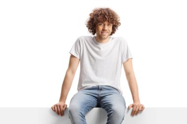 Beyaz arka planda boş bir panelde oturan kıvırcık saçlı adam.