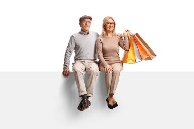 Alışveriş torbaları olan olgun bir çift beyaz arka planda boş bir panelde oturuyor.