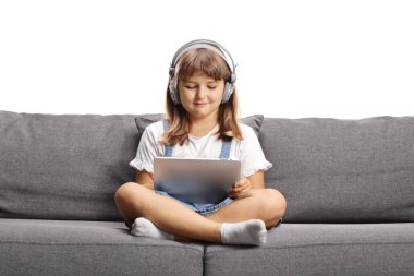Koltuğunda oturan ve beyaz arka planda izole edilmiş tablet kullanan kulaklıklı bir çocuk.