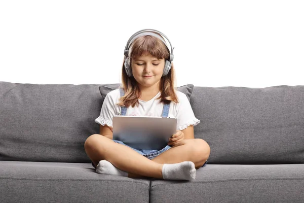 Koltuğunda oturan ve beyaz arka planda izole edilmiş tablet kullanan kulaklıklı bir çocuk.