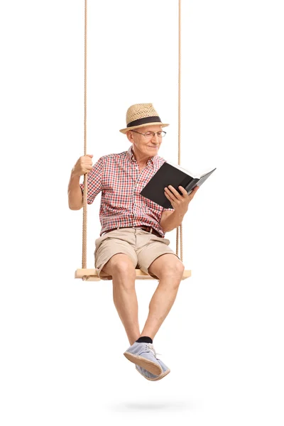 Senior man on swing reading a book — Stock fotografie