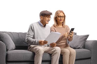 Kanepede oturan yaşlı çift, beyaz arka planda izole edilmiş akıllı telefon ve belgeler kullanıyorlar.