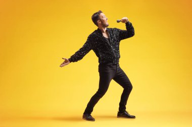 Showman sarı arka planda bir mikrofona şarkı söylüyor.