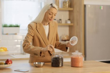 Mutfakta bir kadın, kavanozdan fasulye ve mercimek topluyor.