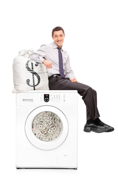 Businessman sitting on washing machine full of money — Stock Fotó