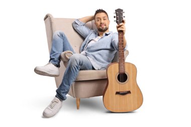 Rahat bir adam beyaz arka planda izole edilmiş akustik gitarla koltukta oturuyor.