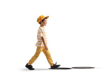 Sarı şapkalı bir çocuğun beyaz arka planda izole edilmiş bir rögar kapağının yanından geçerken tam boy profil fotoğrafı.