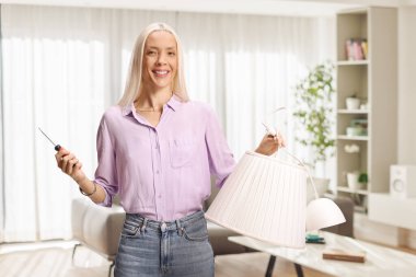 Ev dekorasyonu için elinde abajur ve tornavida tutan mutlu kadın.