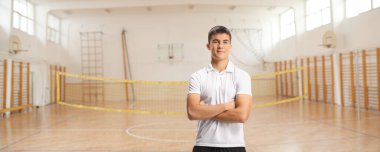 Spor salonunda beyaz tişörtlü ve eşofmanlı bir erkek sporcu poz veriyor.