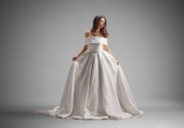 Gelinliğini gri arka planda tutan zarif gelin.