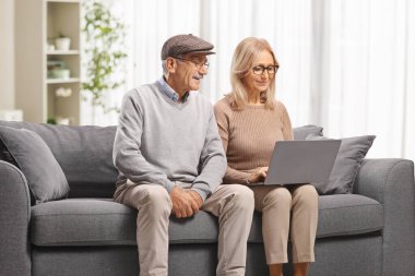 Olgun bir erkek ve kadın kanepede oturuyor ve evdeki dizüstü bilgisayarda çalışıyor.