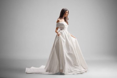 Gelin omuzdan zarif bir elbise giyer. Parlak bir gelinlik. Zemin uzunluğunda.