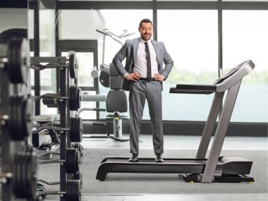 Takım elbiseli ve kravatlı bir iş adamı spor salonunda koşu bandında dikiliyor.