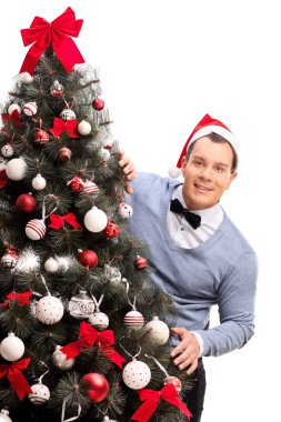 Man with Santa hat behind a Christmas tree