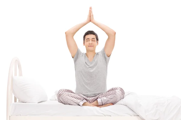 Young man meditating seated on a bed — Stock Photo, Image
