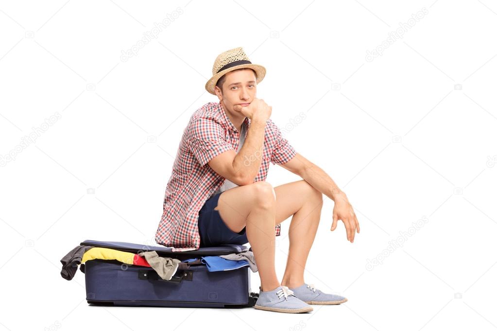 Sad male tourist sitting on bag full of clothes 