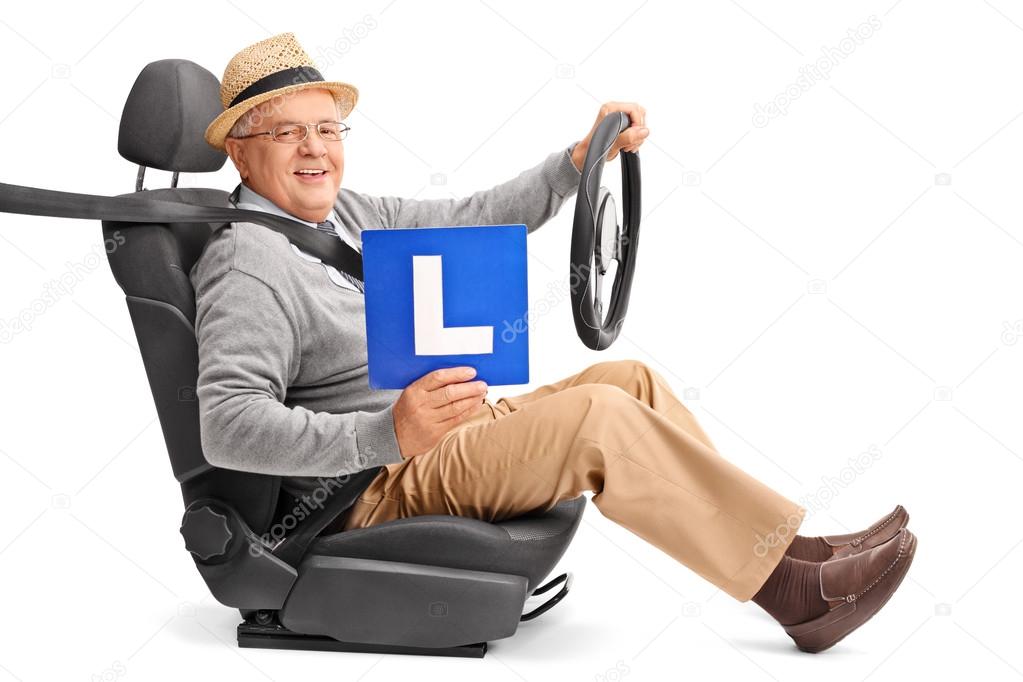 Senior gentleman sitting on a car seat and holding an L-sign isolated on white background