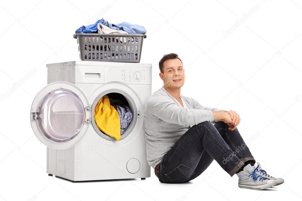 Young man sitting by a washing machine 