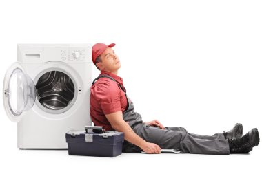 Exhausted plumber sitting by a washing machine clipart