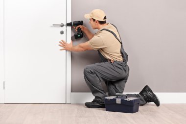 Young locksmith installing a lock on a door clipart
