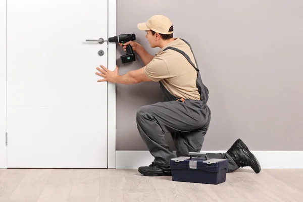 Joven cerrajero instalando una cerradura en una puerta Imágenes De Stock Sin Royalties Gratis