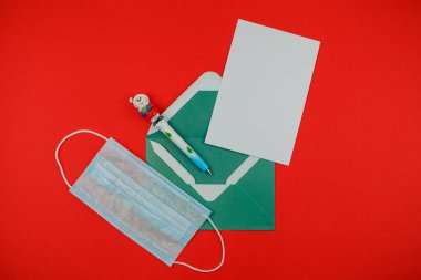 Kırmızı arkaplanda bir mektup ve tıbbi maske olan bir zarf. Noel Baba 'ya Noel mektubu.