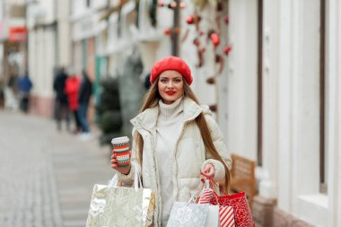 Güzel genç bayan Noel alışverişi yapıyor. Bir Avrupa şehrinin caddesinde kırmızı bereli genç bir kadının portresi..