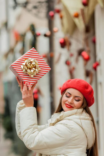 在欧洲城市的大街上 一个戴着红色贝雷帽的年轻女子的画像 手里拿着礼品盒 圣诞购物 — 图库照片