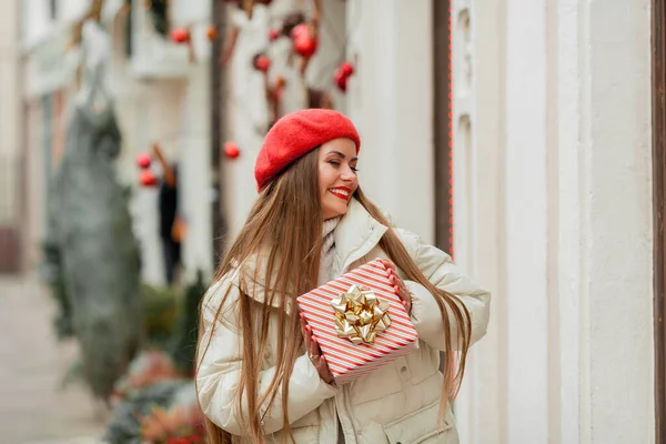 在欧洲城市的大街上 一个戴着红色贝雷帽的年轻女子的画像 手里拿着礼品盒 圣诞购物 — 图库照片