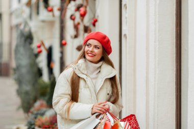Güzel genç bayan Noel alışverişi yapıyor. Bir Avrupa şehrinin caddesinde kırmızı bereli genç bir kadının portresi..