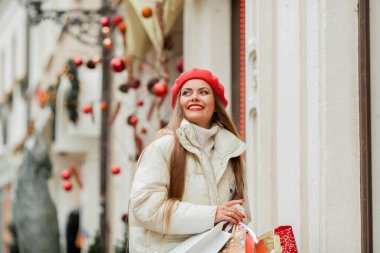 Güzel genç bayan Noel alışverişi yapıyor. Bir Avrupa şehrinin caddesinde kırmızı bereli genç bir kadının portresi..