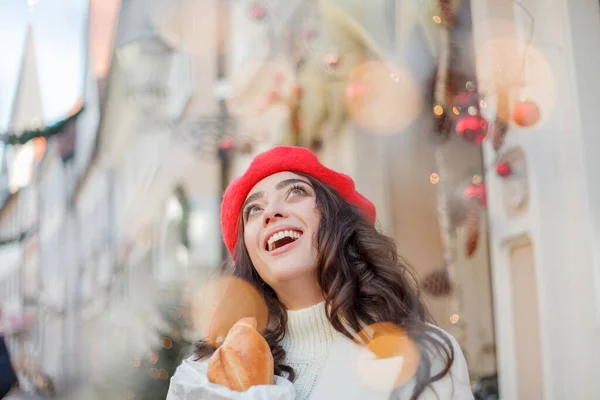在欧洲的一个城市 一个年轻美丽的女人穿着红色贝雷帽的画像 年轻的女人拿着一个纸袋和面包 圣诞节 — 图库照片