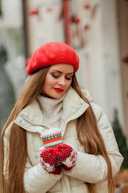 Avrupa 'da bir kentte elinde Noel kahvesi kupası olan kırmızı bereli güzel bir kadın. Tatiller.