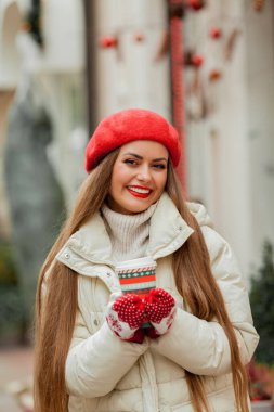 Avrupa 'da bir kentte elinde Noel kahvesi kupası olan kırmızı bereli güzel bir kadın. Tatiller.