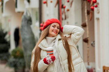 Avrupa 'da bir kentte elinde Noel kahvesi kupası olan kırmızı bereli güzel bir kadın. Tatiller.