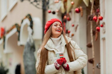 Avrupa 'da bir kentte elinde Noel kahvesi kupası olan kırmızı bereli güzel bir kadın. Tatiller.