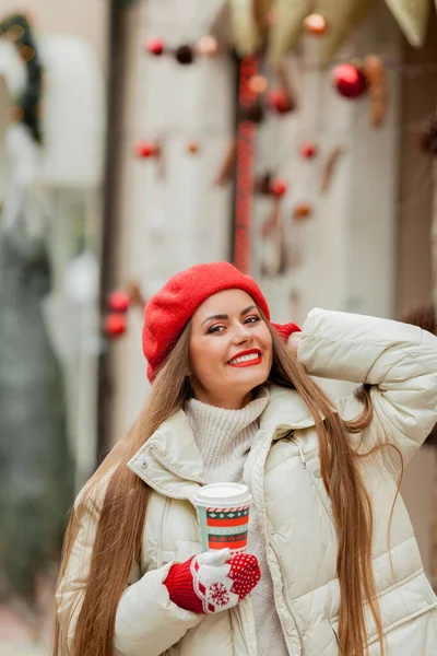 在欧洲的一个城市 年轻美丽的女人戴着红色贝雷帽 手里拿着圣诞咖啡杯 — 图库照片
