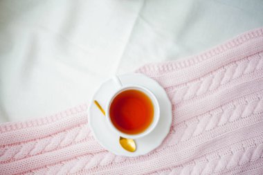 Bir kupa sıcak çay, yatağın üzerine pembe bir ekose örgü. Yatakta kahvaltı. Samimi. Bahar.
