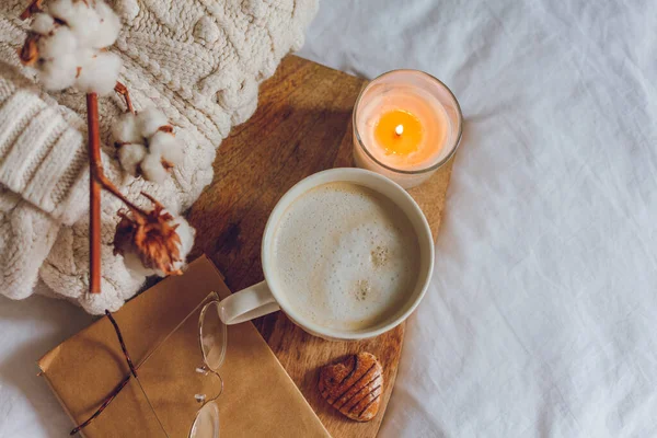 Zuhause gemütlich eingerichtet. Ein Becher Cappuccino, Kekse, eine Kerze auf dem Bett. Wintermorgen. — Stockfoto