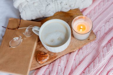 Örgü süveter, pembe ekose, mum, kapuçino kupası, kitap, yatakta gözlük. Sıcak bir kahvaltı. Kış. Sonbahar.