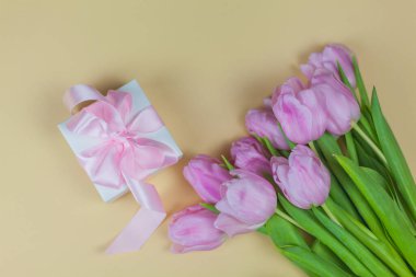 Kurdeleli hediye kutusu, bej arka planda pembe laleler. Anneler Günü. Uluslararası Kadınlar Günü.