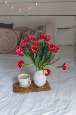 Yatakta kahvaltı. Bir kupa kahve, vazoda bir buket lale, ahşap tepsi. Kadınlar Günü. Bahar. Samimi.