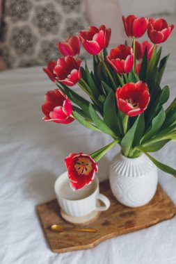 Yatakta kahvaltı. Bir kupa kahve, vazoda bir buket lale, ahşap tepsi. Kadınlar Günü. Bahar. Samimi.