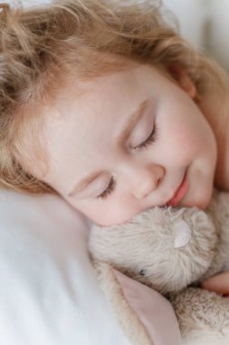 Uyuyan ve peluş tavşanına sarılan küçük bir kızın yakın çekimi. Rahatlama. İyi uykular. Samimi.