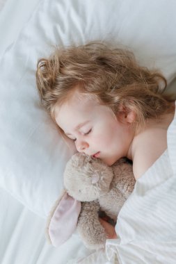 Uyuyan ve peluş tavşanına sarılan küçük bir kızın yakın çekimi. Rahatlama. İyi uykular. Samimi.