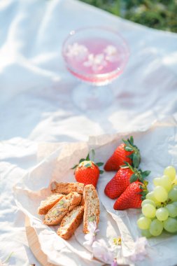 Doğada bahar pikniği. Bir bardak pembe şampanya, sakura çiçekleri, hasır bir çanta, bir şapka, İtalyan..