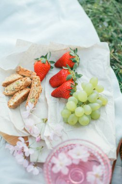 Doğada bahar pikniği. Bir bardak pembe şampanya, sakura çiçekleri, hasır bir çanta, bir şapka, İtalyan..