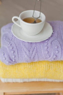 Tahta bir sandalyeye bir yığın bahar örgü giysileri çay yapraklı bir kupa sıcak çay. Sarı, mor renkler.