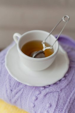 Tahta bir sandalyeye bir yığın bahar örgü giysileri çay yapraklı bir kupa sıcak çay. Sarı, mor renkler.