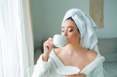 Duştan sonra, kafasında havlu olan bornozlu genç bir kadın kahve içer ve pencereden dışarı bakar. - Günaydın. Kahvaltı..